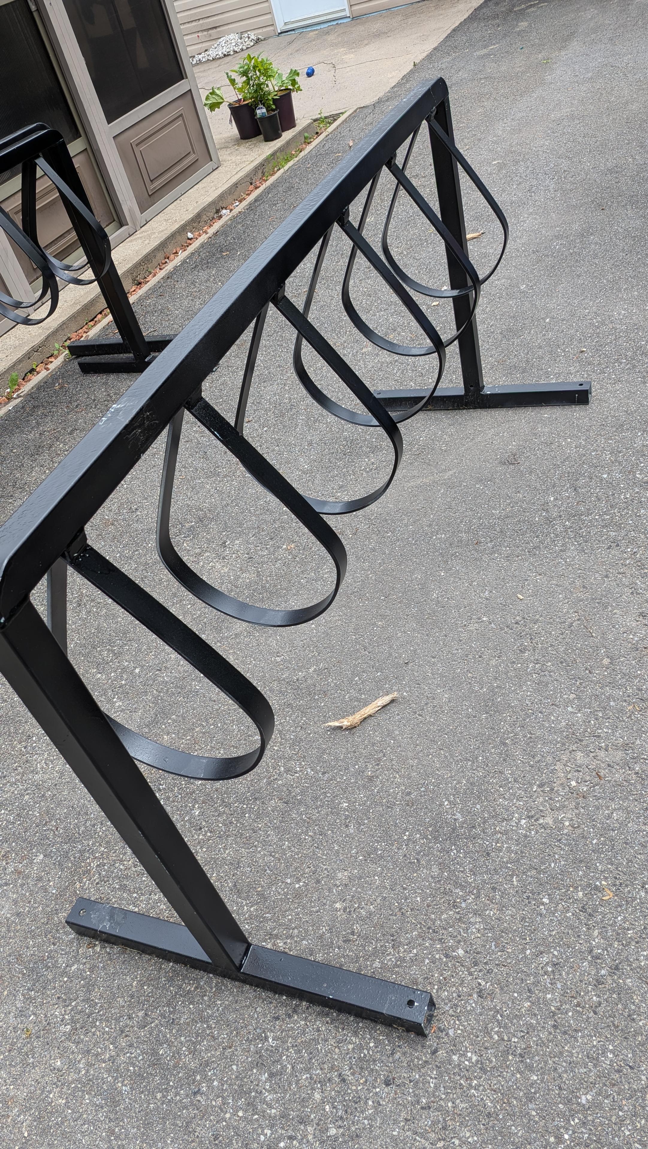 A black bike rack, about seven feet long and 2½ feet high, with six teardrop loops.